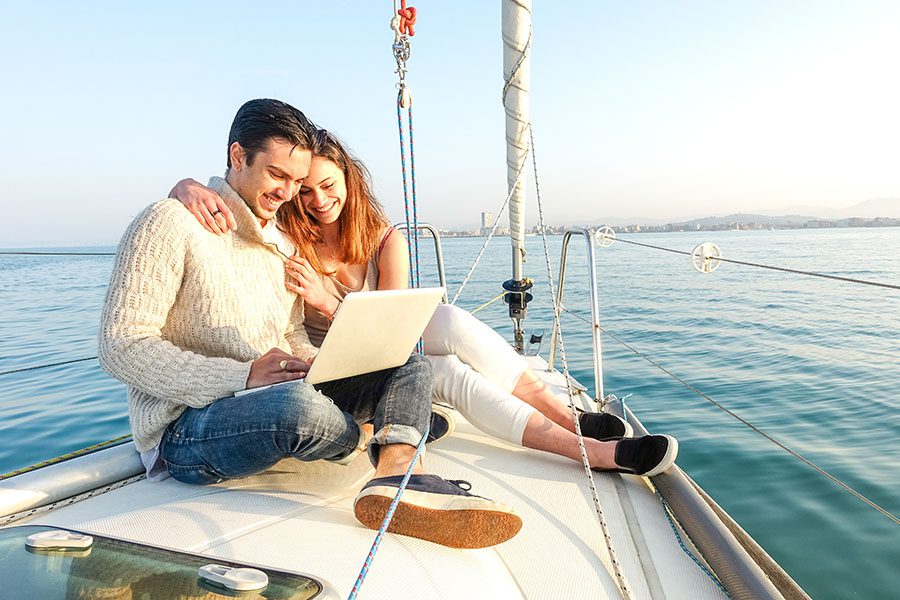 Client Center - Young Couple Sitting On Yacht At Sea Using Laptop
