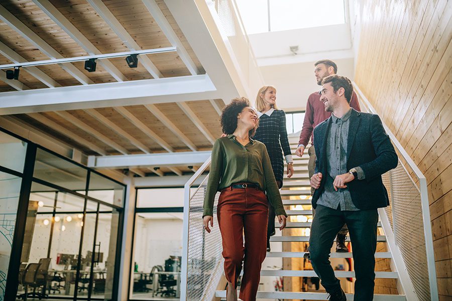 Employee Benefits - Group Of Employees Smiling While Walking Down Stairs In Modern Office