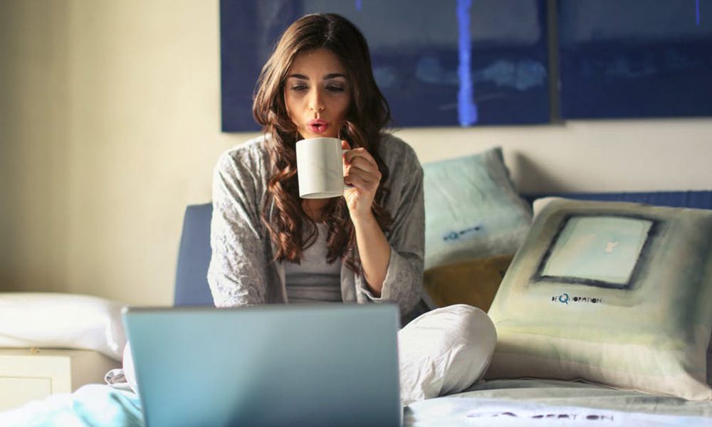 Blog - Single Woman Enjoying a Cup of Coffee on Her Bed While She Uses Her Laptop