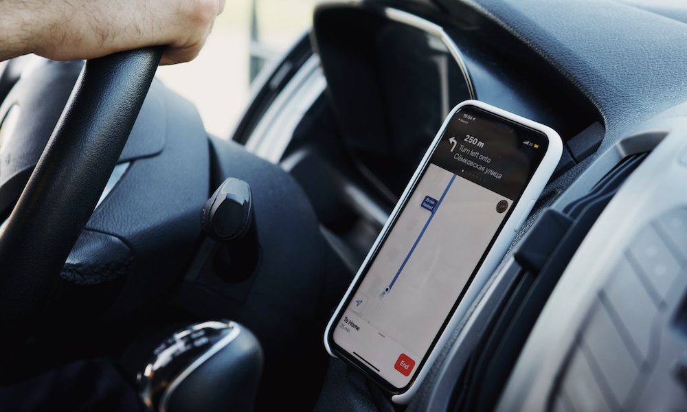 Image of a person driving a car with a smartphone app open on their phone on the dashboard while driving.